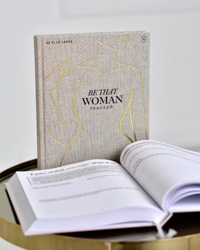 Be That Woman tervező, előtte egy nyitott példány arany asztalkán