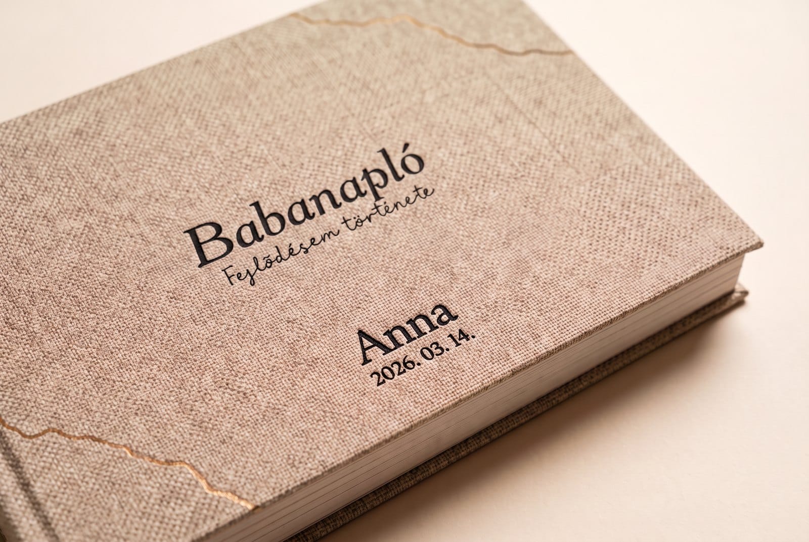Natúr lenvászon Babanapló borító, a cím alatt kicsi, fekete gravírozás: Anna és 2026. 03. 14.